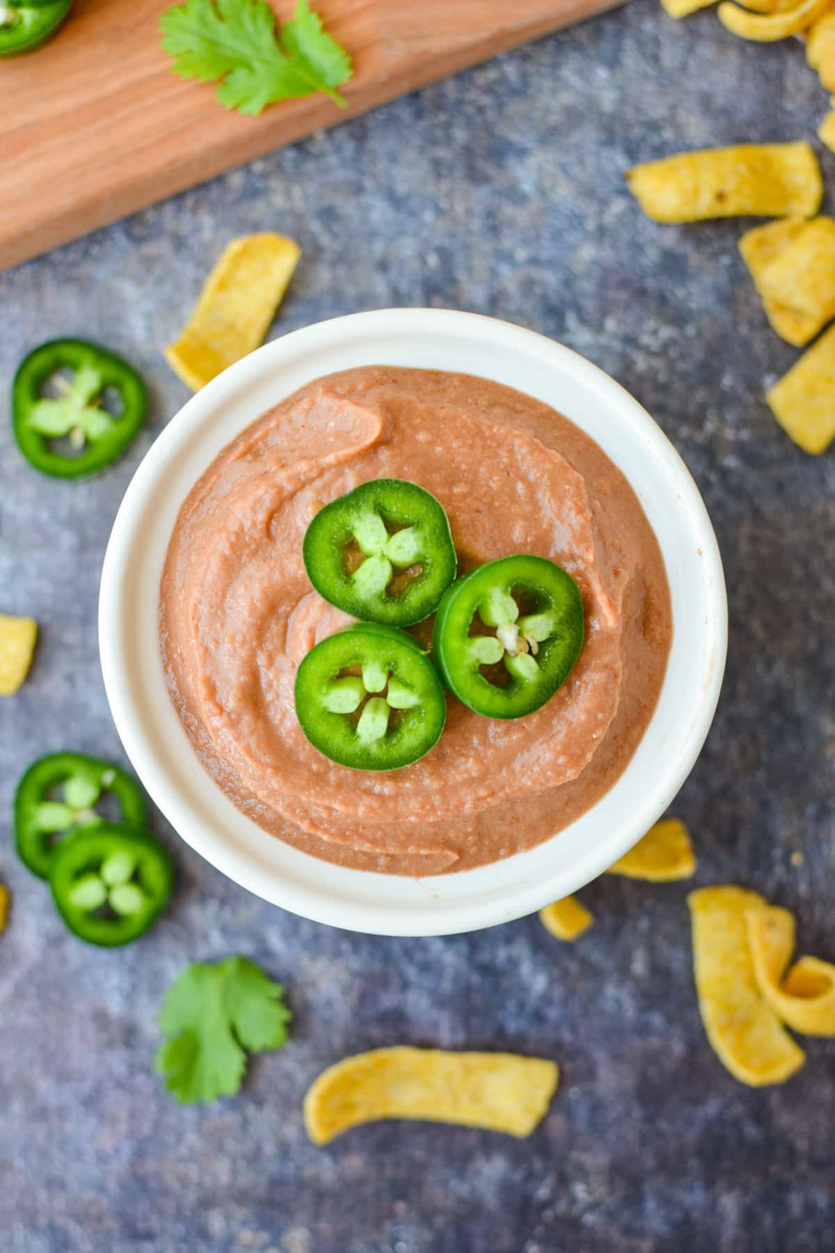 A bowl of bean dip garnished with jalapeno slices on top.