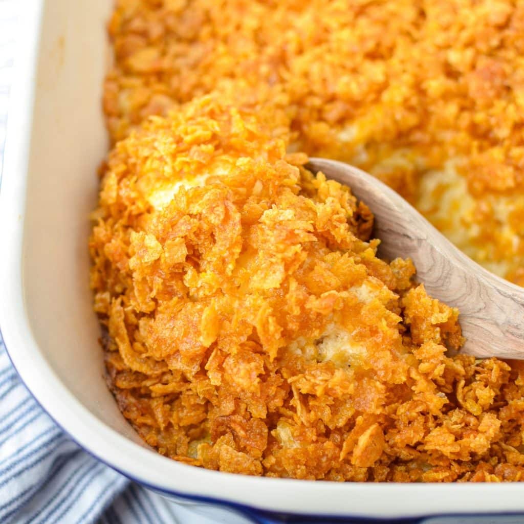 Scooping a small amount of hash brown casserole with a wooden spoon.