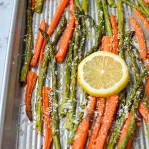 A sheet pan with roasted carrots and asparagus, garnished with lemon slices.