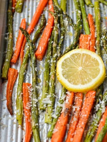 A sheet pan with roasted carrots and asparagus, garnished with lemon slices.