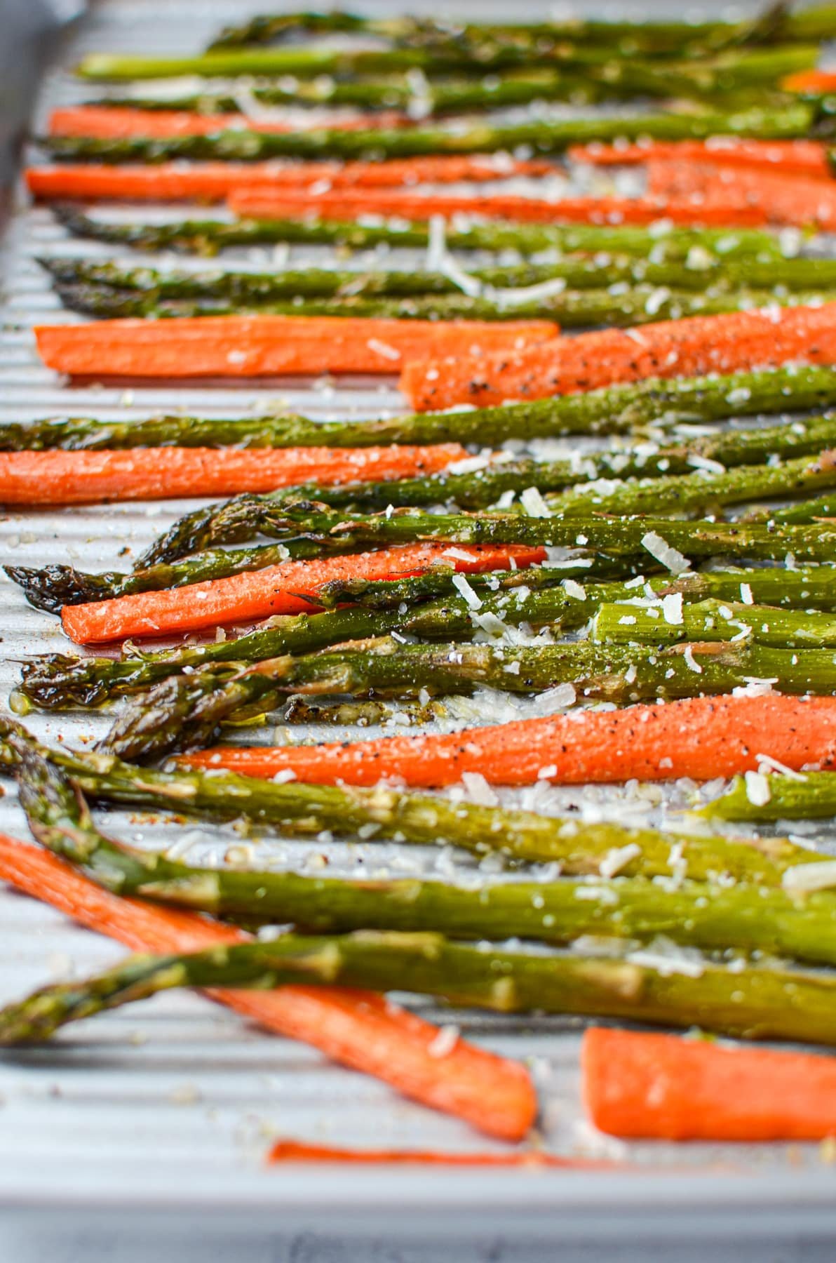 A sheet pan with roasted asparagus and carrots, garnished with parmesan cheese.