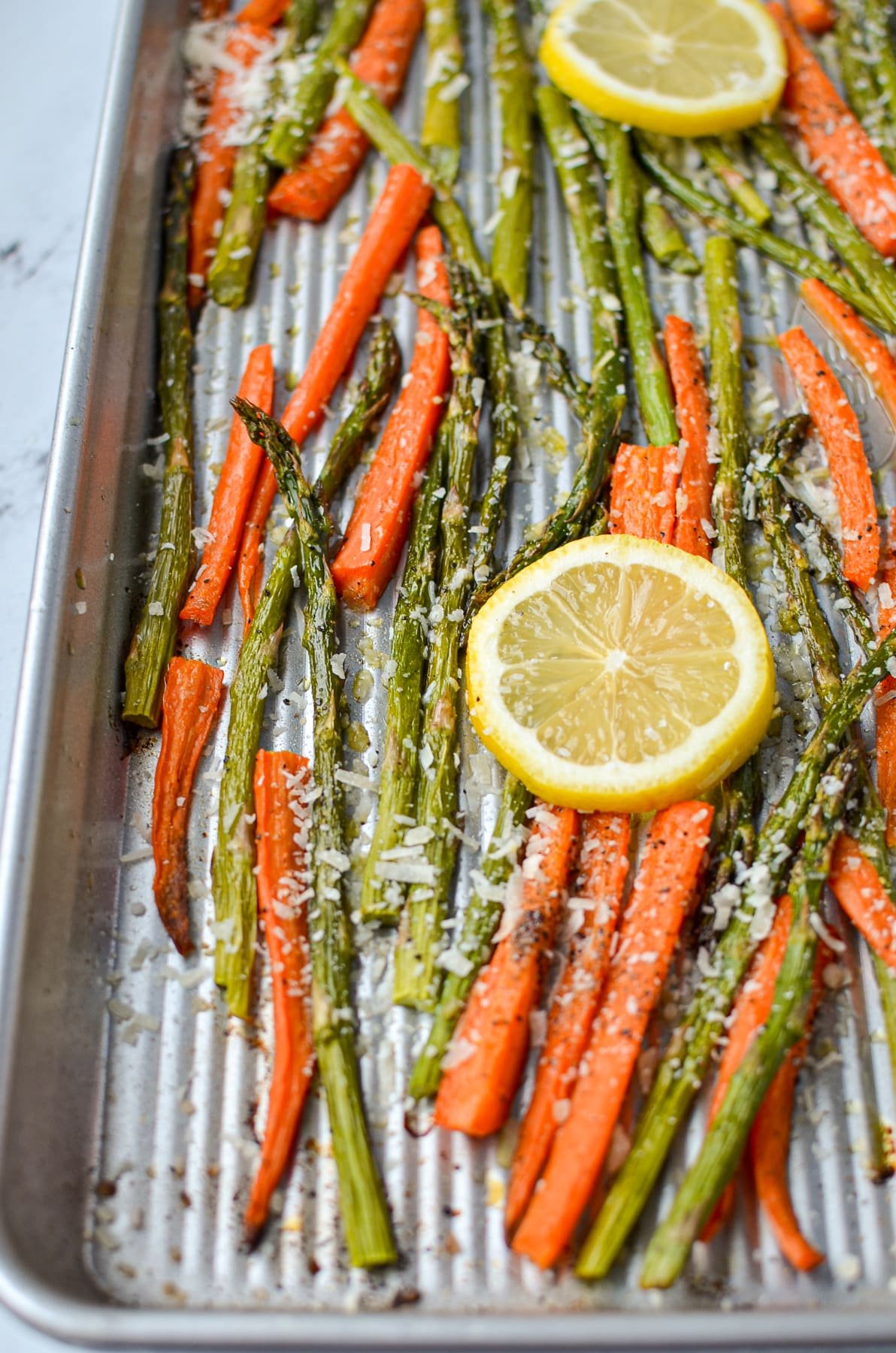 A sheet pan with asparagus and carrots, garnished with lemon slices.