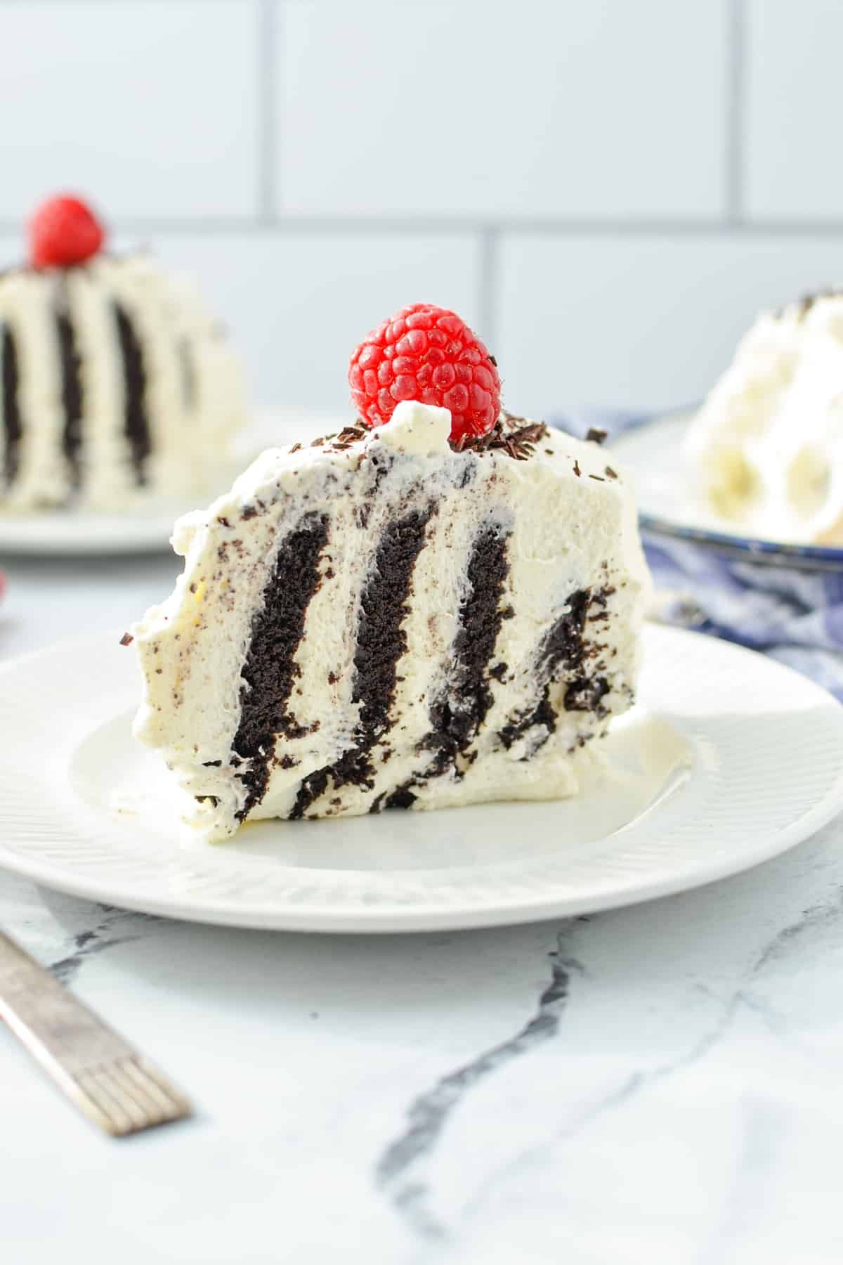 A slice of cake with chocolate wafers, garnished with a fresh raspberry on top.