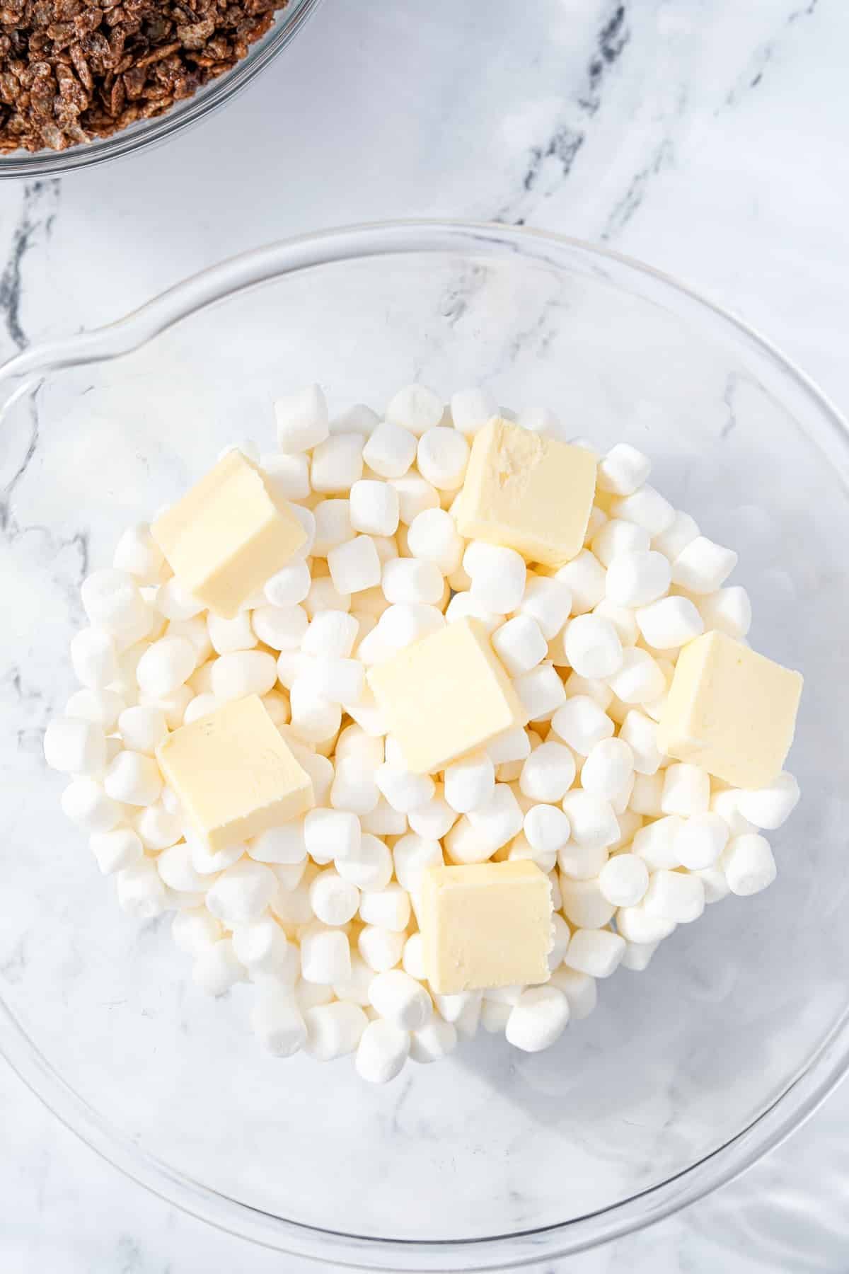A bowl of mini marshmallows with cubed butter on top.
