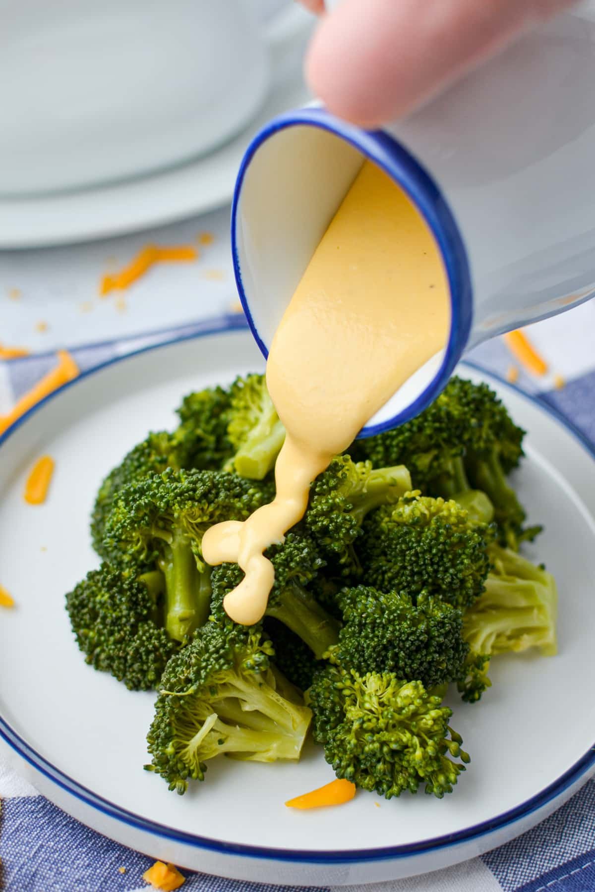 Drizzling cheese sauce on top of broccoli.