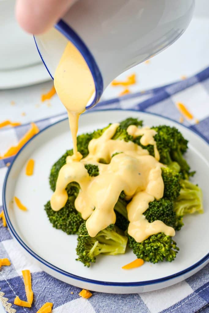 Drizzling cheese sauce on top of broccoli.