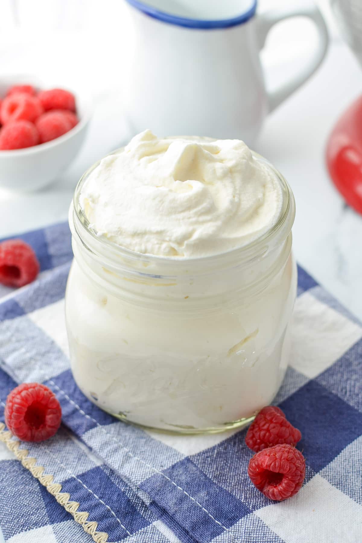 A jar of homemade whipped cream, surrounded by raspberries.