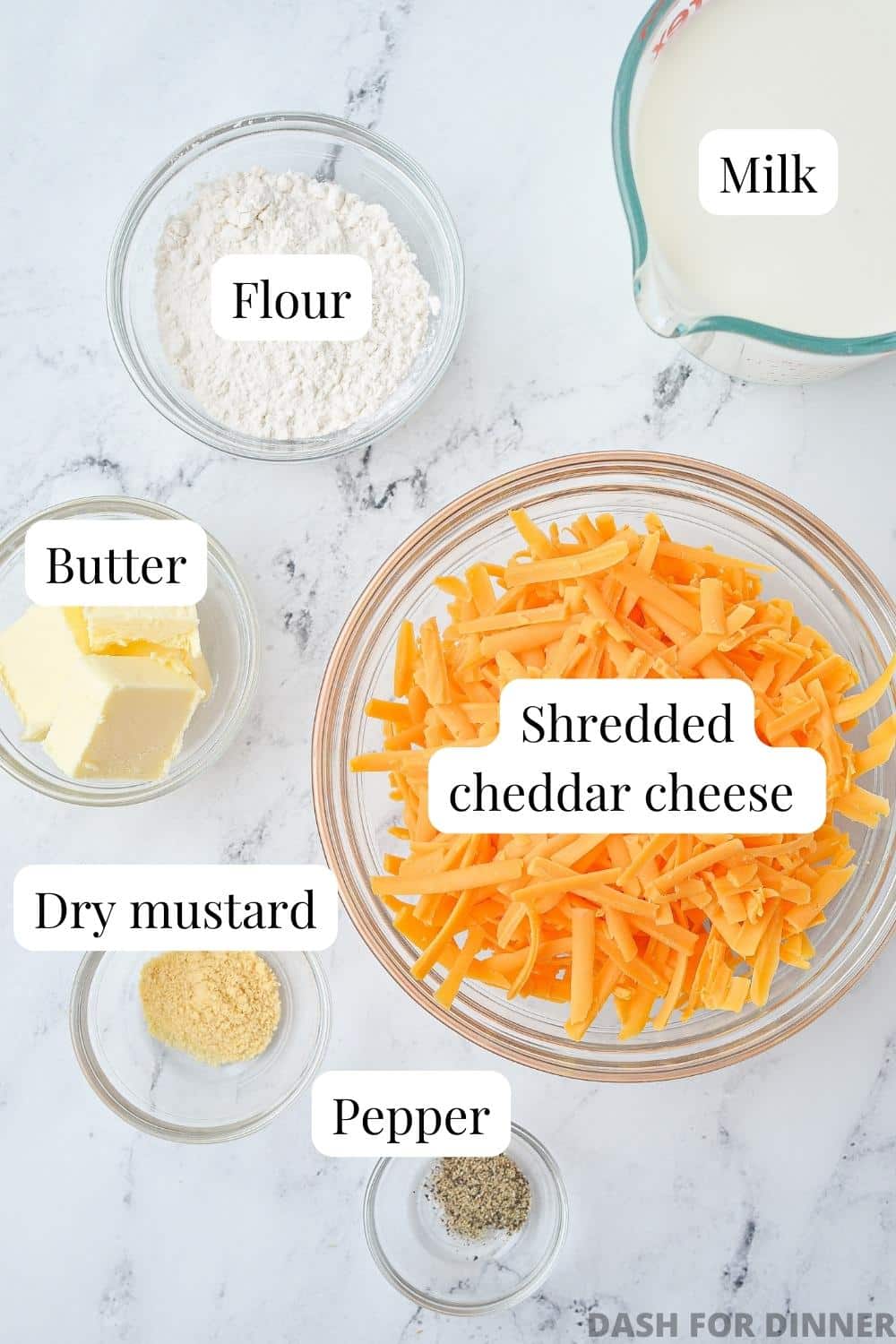 The ingredients needed to make cheese sauce: shredded cheddar, butter, milk, flour, dry mustard, etc.