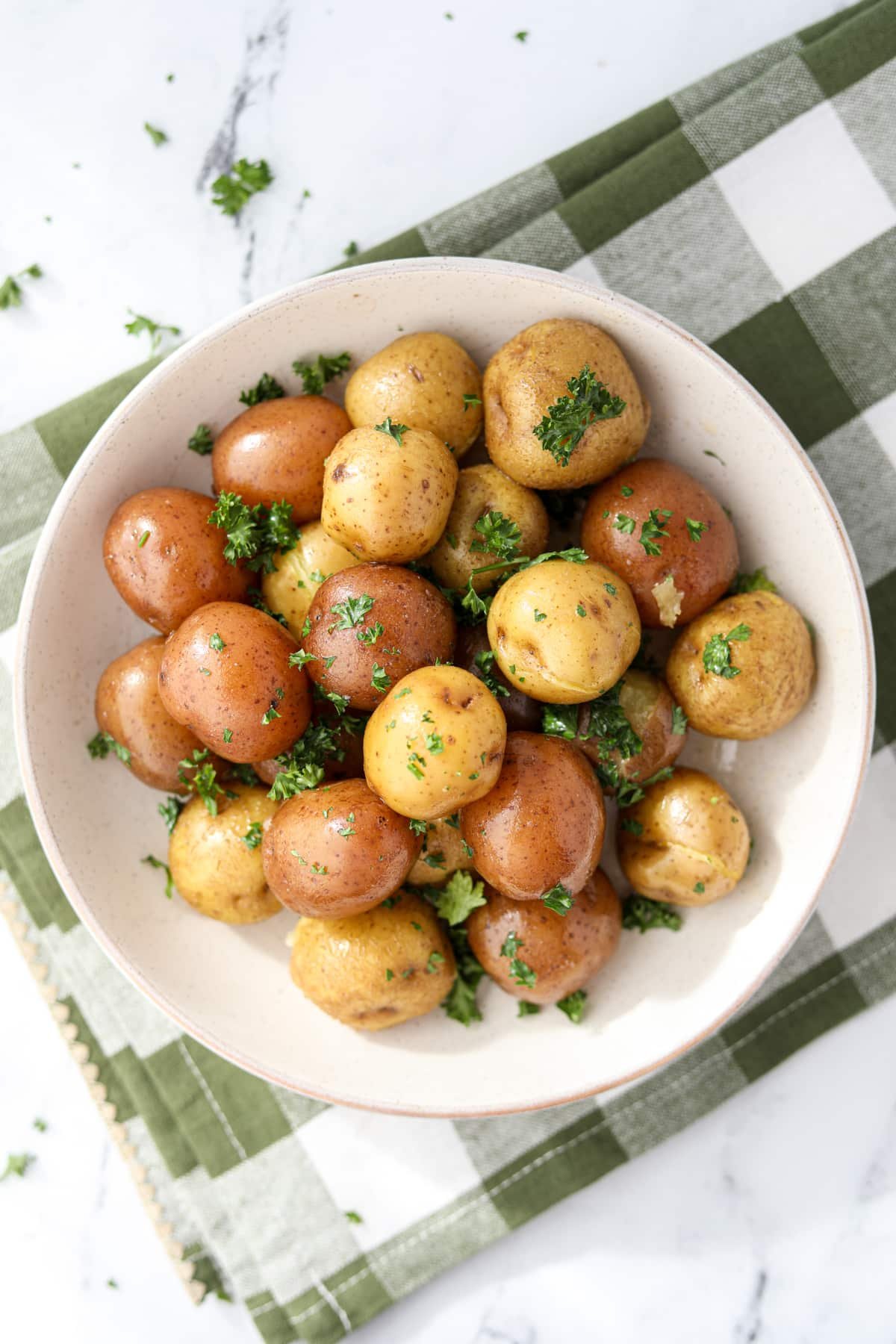 A bowl of buttered baby potatoes garnished with parsley.