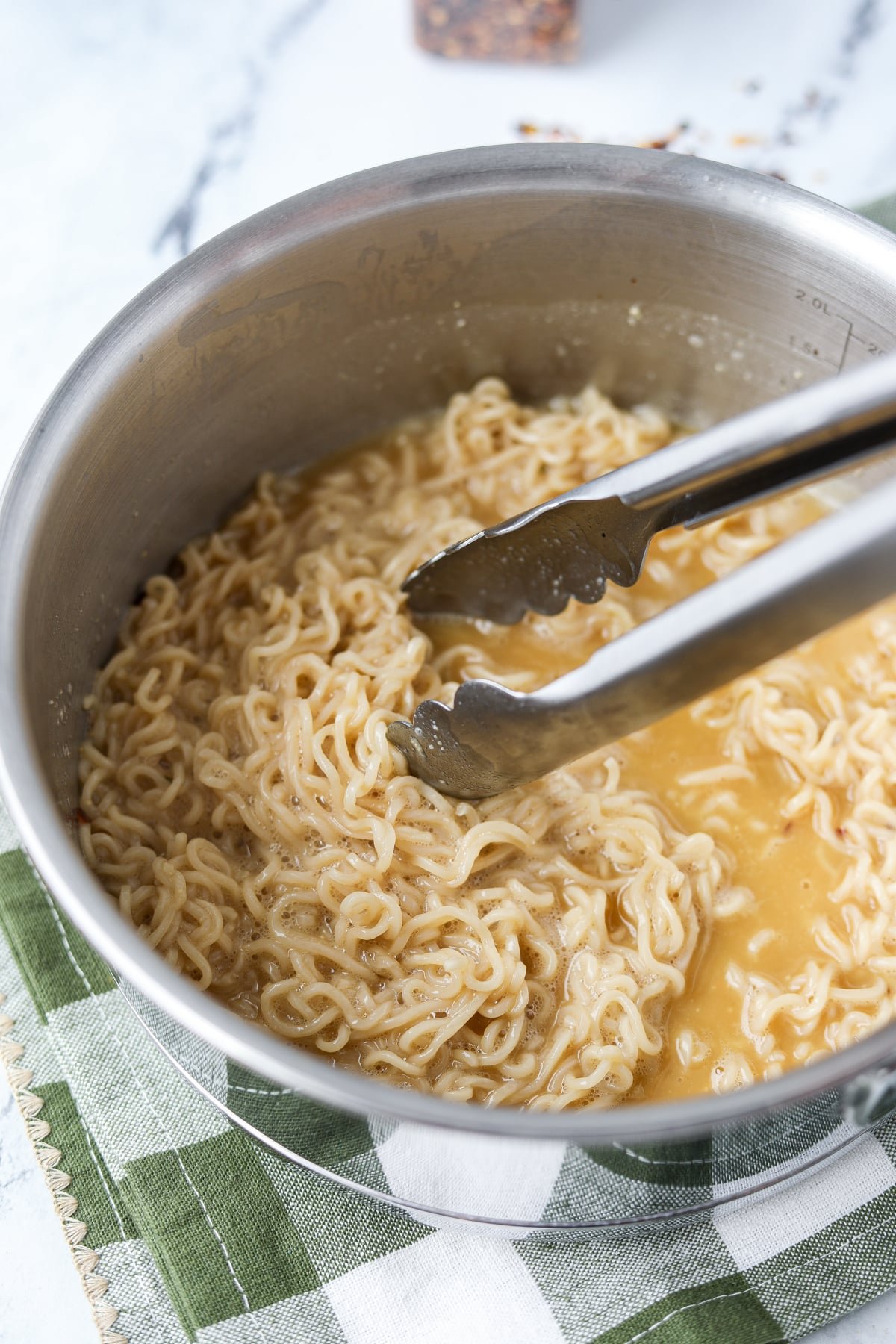 Stirring a skillet of ramen with a creamy sauce.