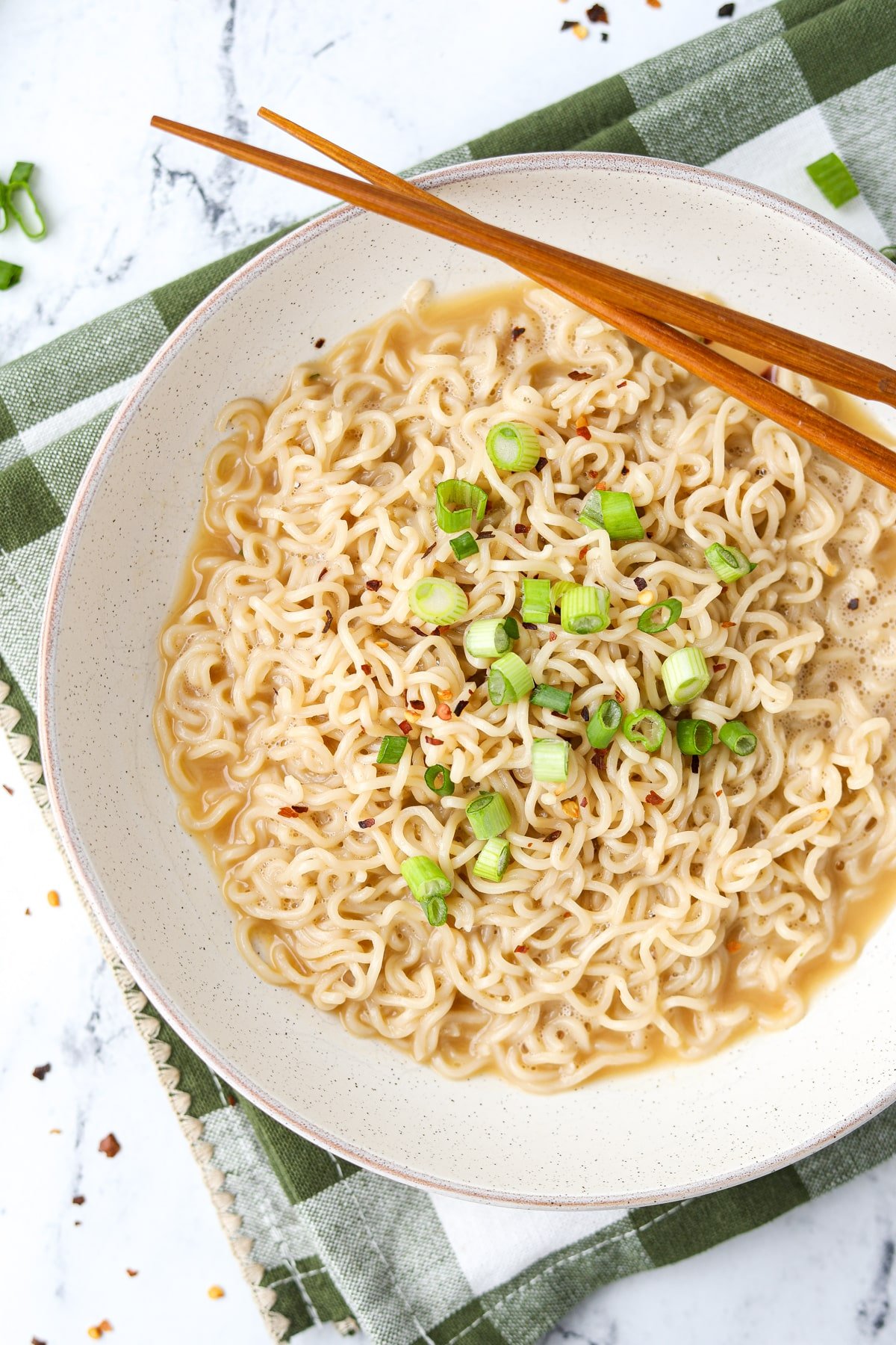 A bowl of ramen garnished with red pepper flakes and green onion.