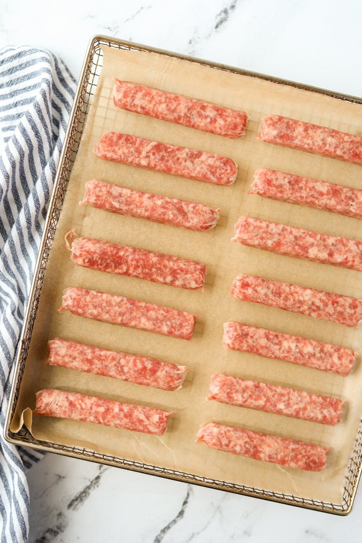 An air fryer tray filled with raw sausage links.