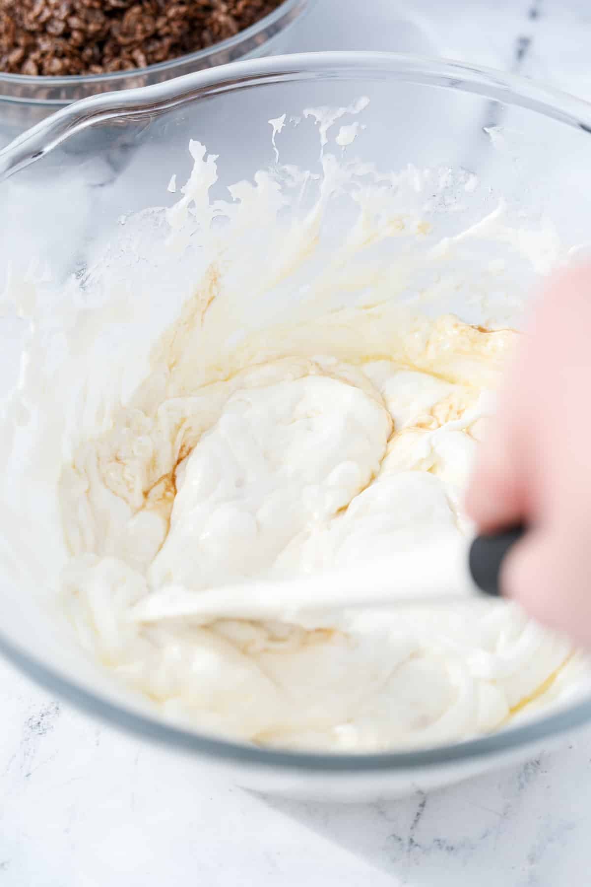 A bowl of melted marshmallows being stirred with vanilla extract added in.