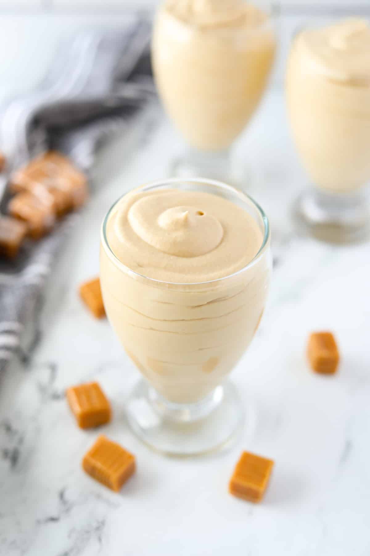 A jar of mousse surrounded by unwrapped caramels.