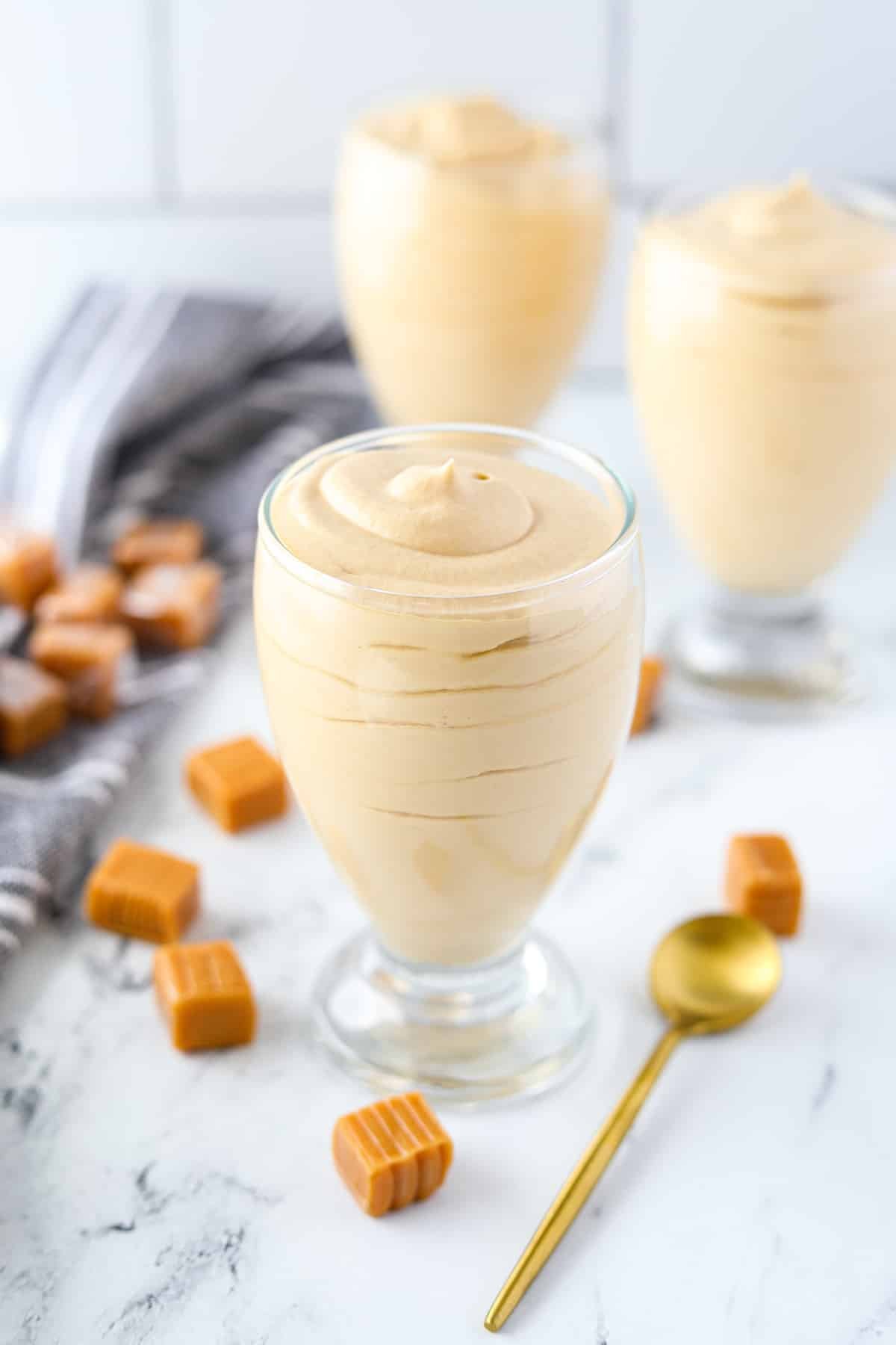 Several dessert glasses surrounded by unwrapped caramels.