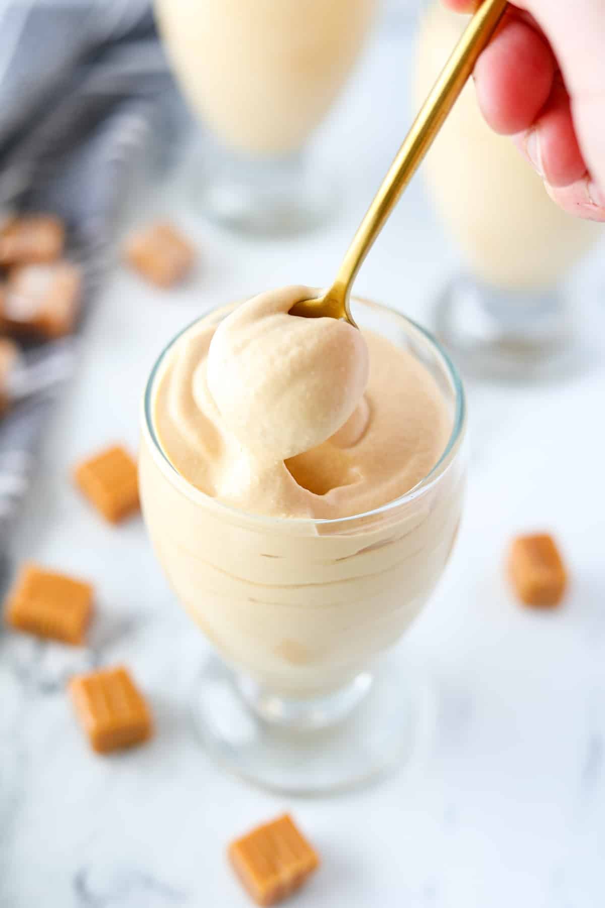 A gold spoon taking a portion of mousse from a glass jar.