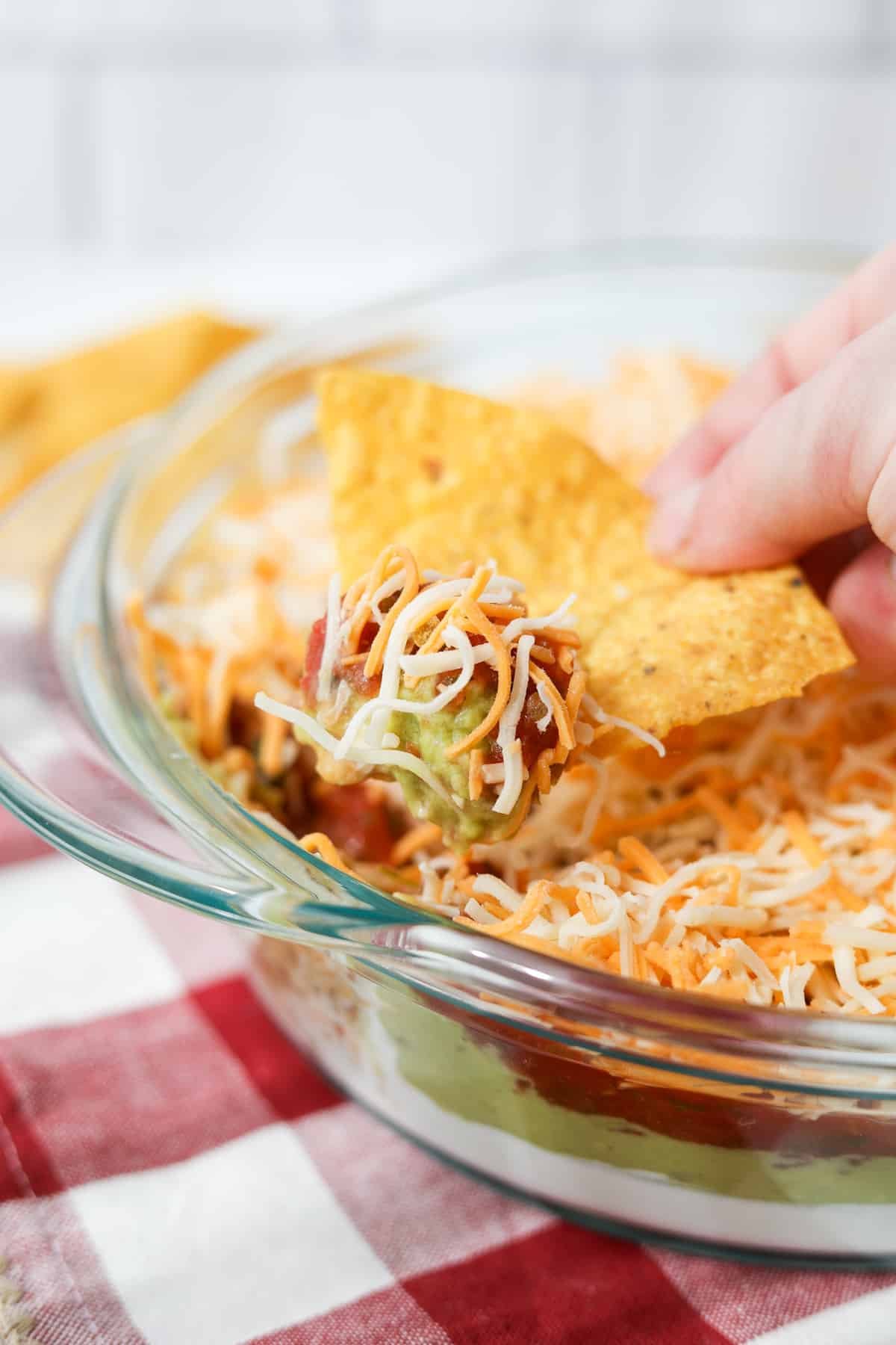 A tortilla chip being dipped into a cold layered dip.