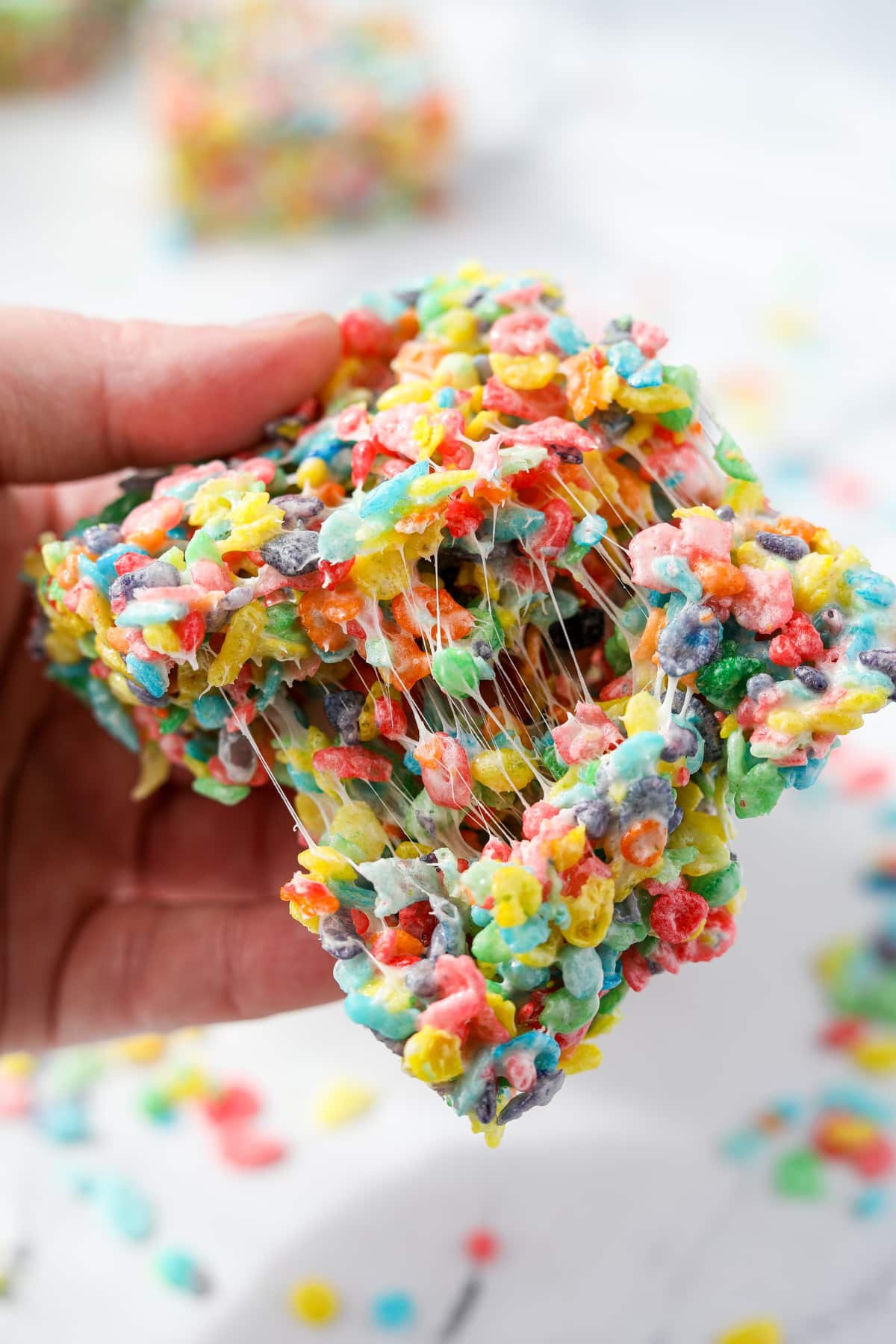 Pulling a Fruity Pebbles cereal treat apart to show the gooey marshmallow.