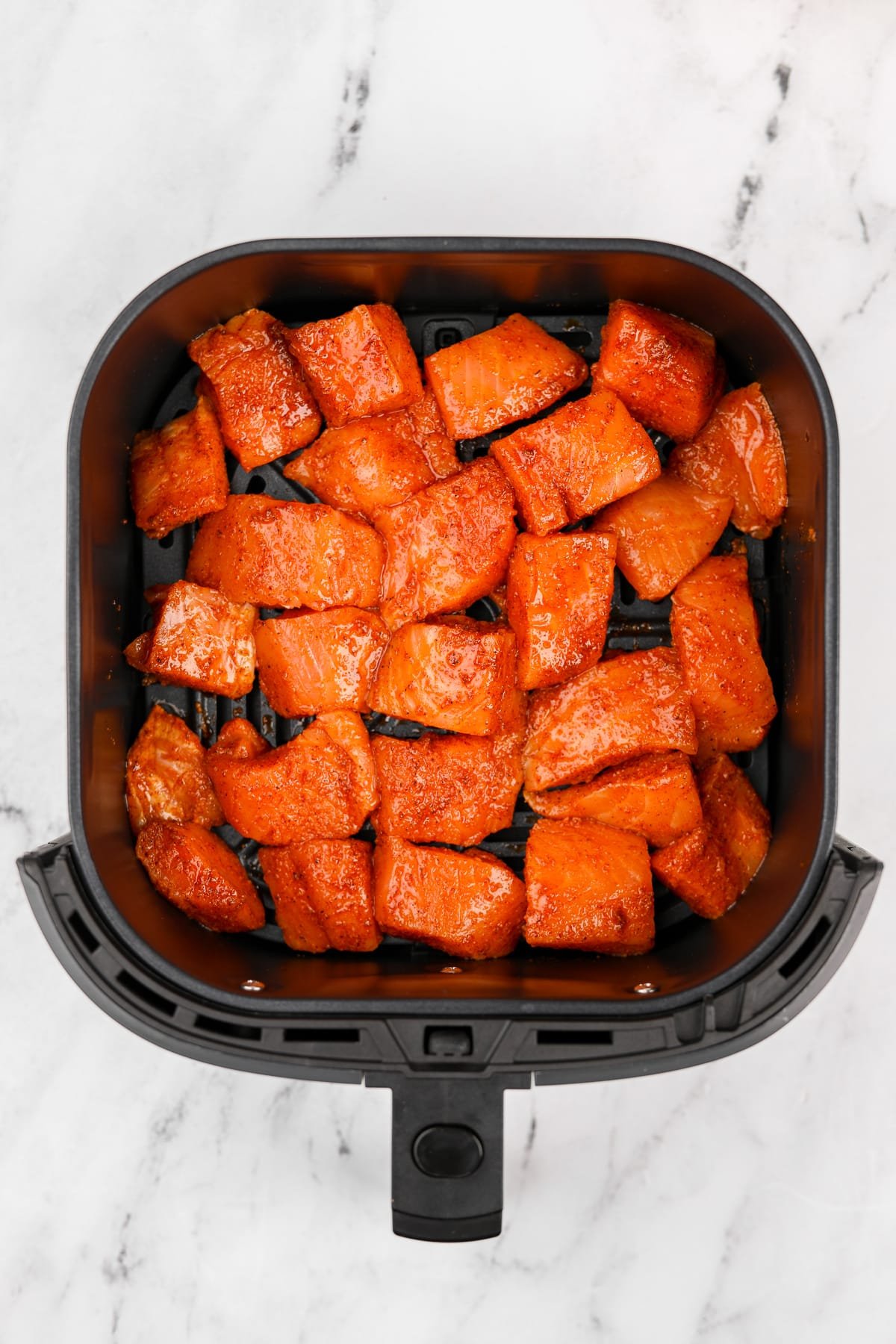 An air fryer basket filled with seasoned salmon chunks.