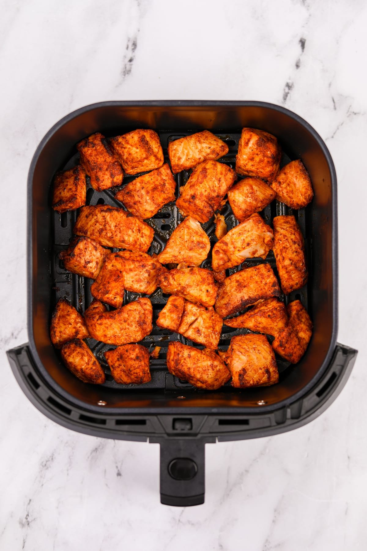 An air fryer basket filled with cooked salmon pieces.