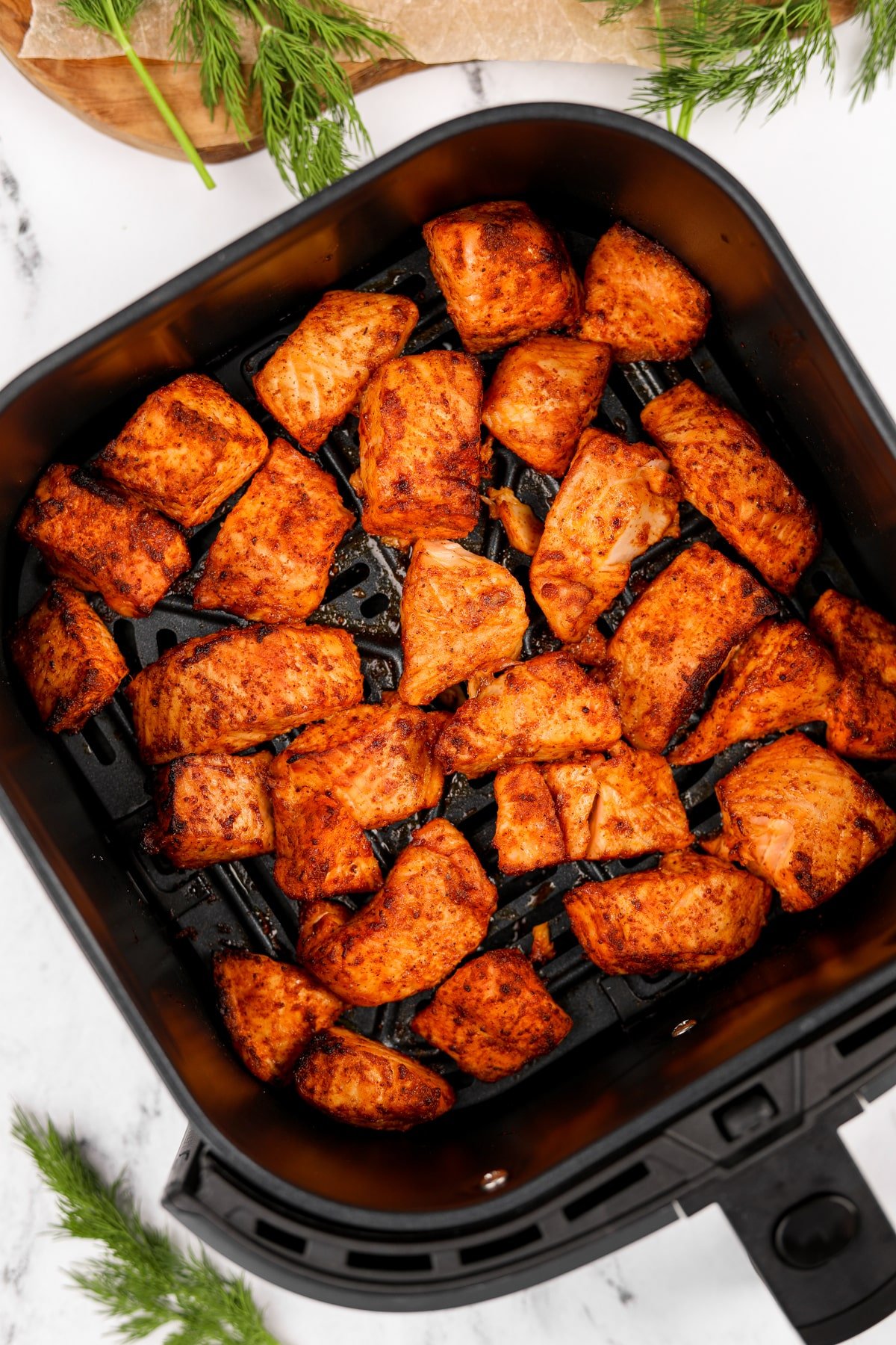 An air fryer basket filled with cubed and cooked salmon.