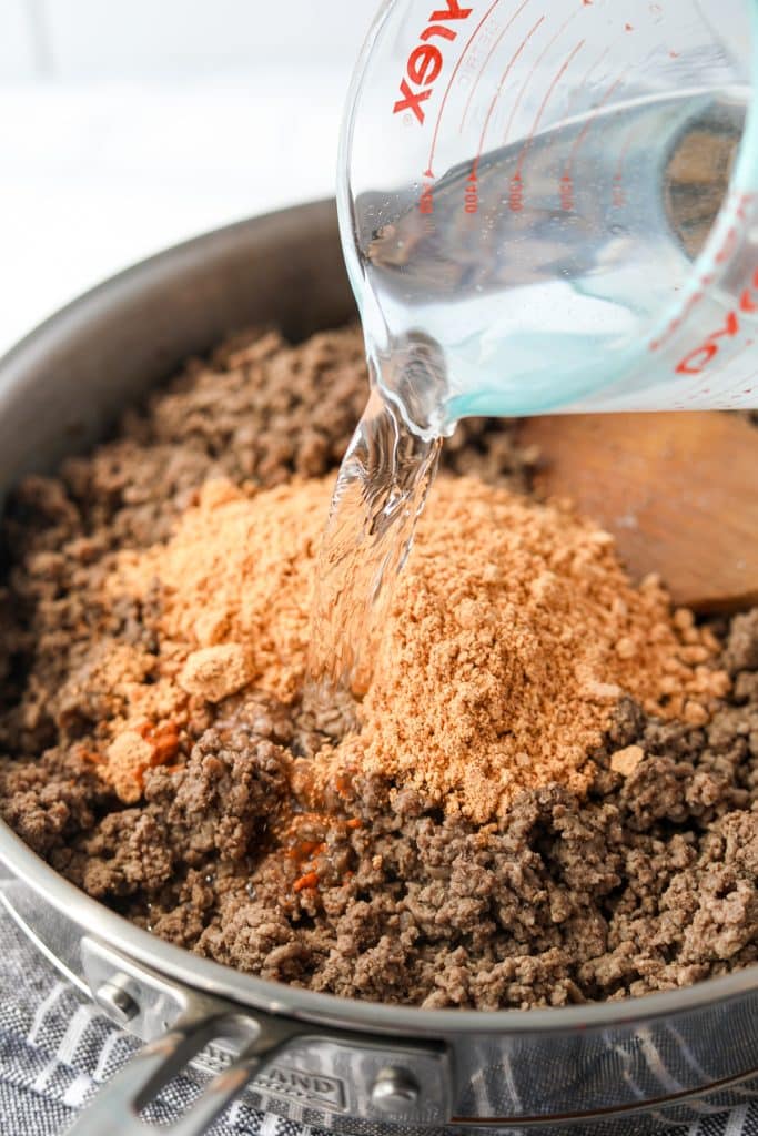 Adding water and taco seasoning to cooked meat.