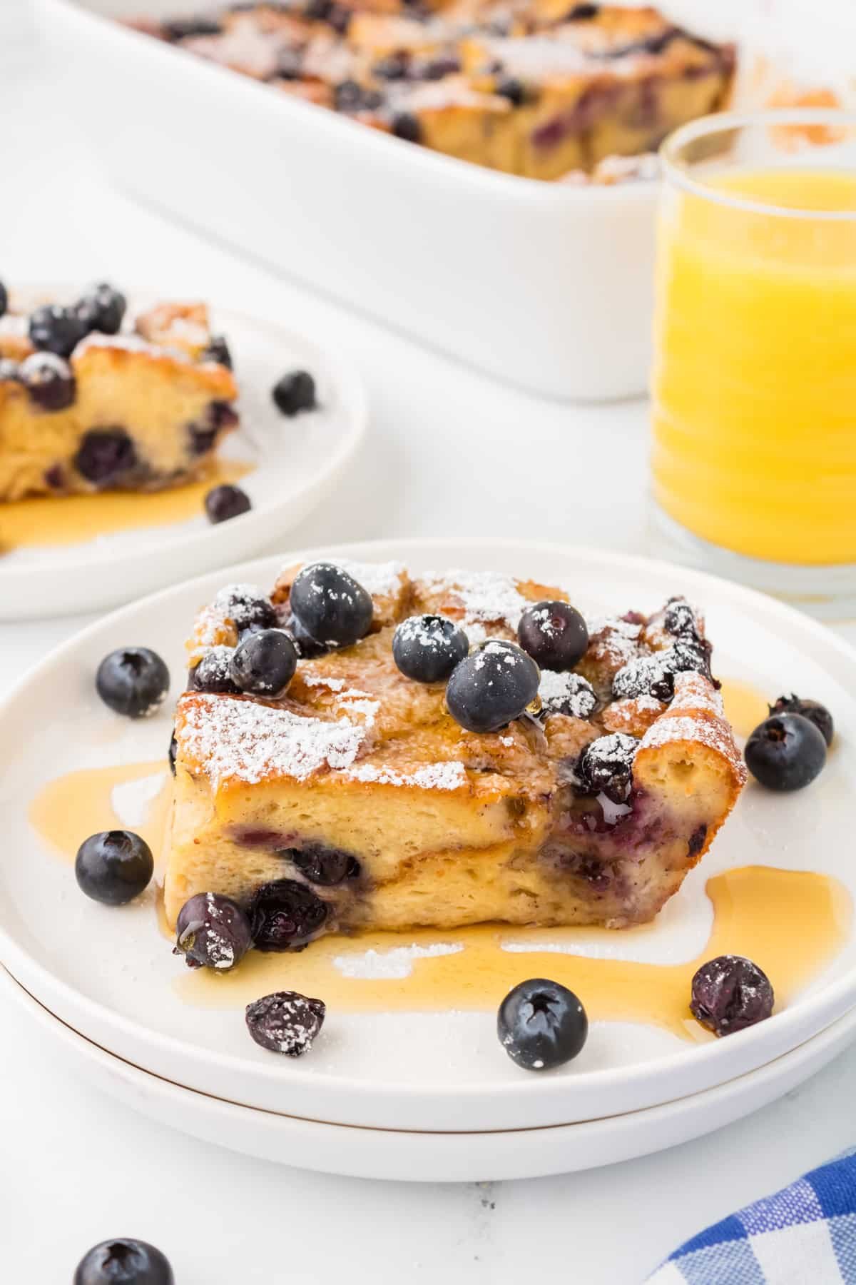 A square of baked brioche French toast garnished with blueberries and drizzled with maple syrup.
