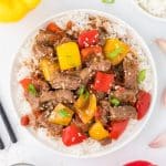 An overhead view of a bowl of pepper steak served with rice and garnished with sesame seeds.