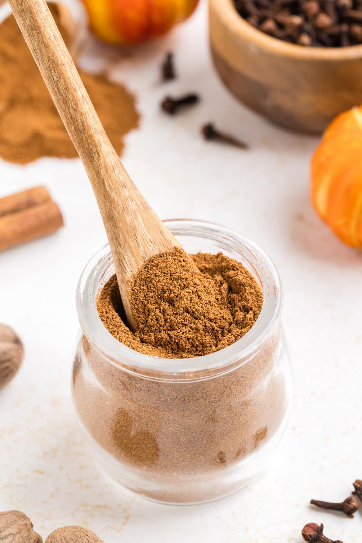 A small wooden spoon taking a portion of pumpkin spice from a small jar.