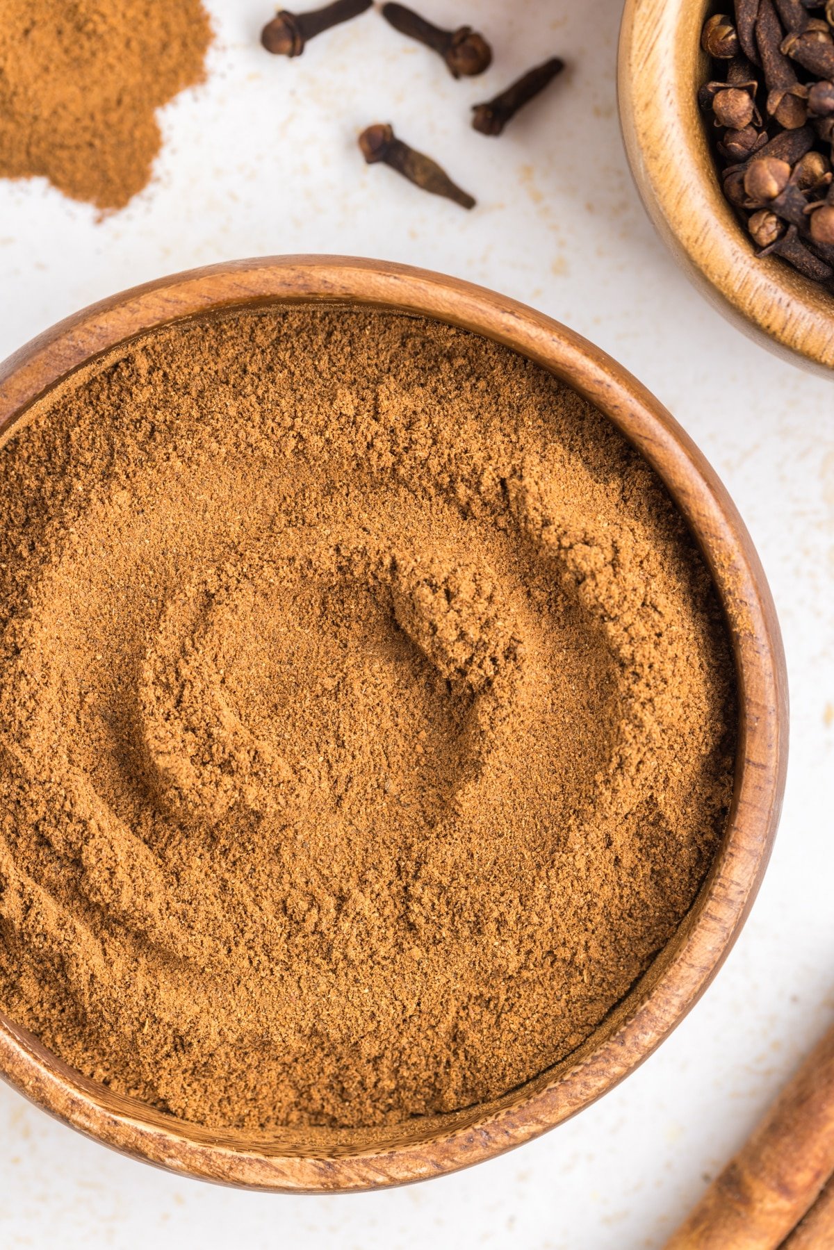 A small bowl of pumpkin spice blend, surrounded by whole cloves and other whole spices.