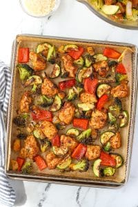An air fryer tray with chicken and vegetables spread in an even layer.