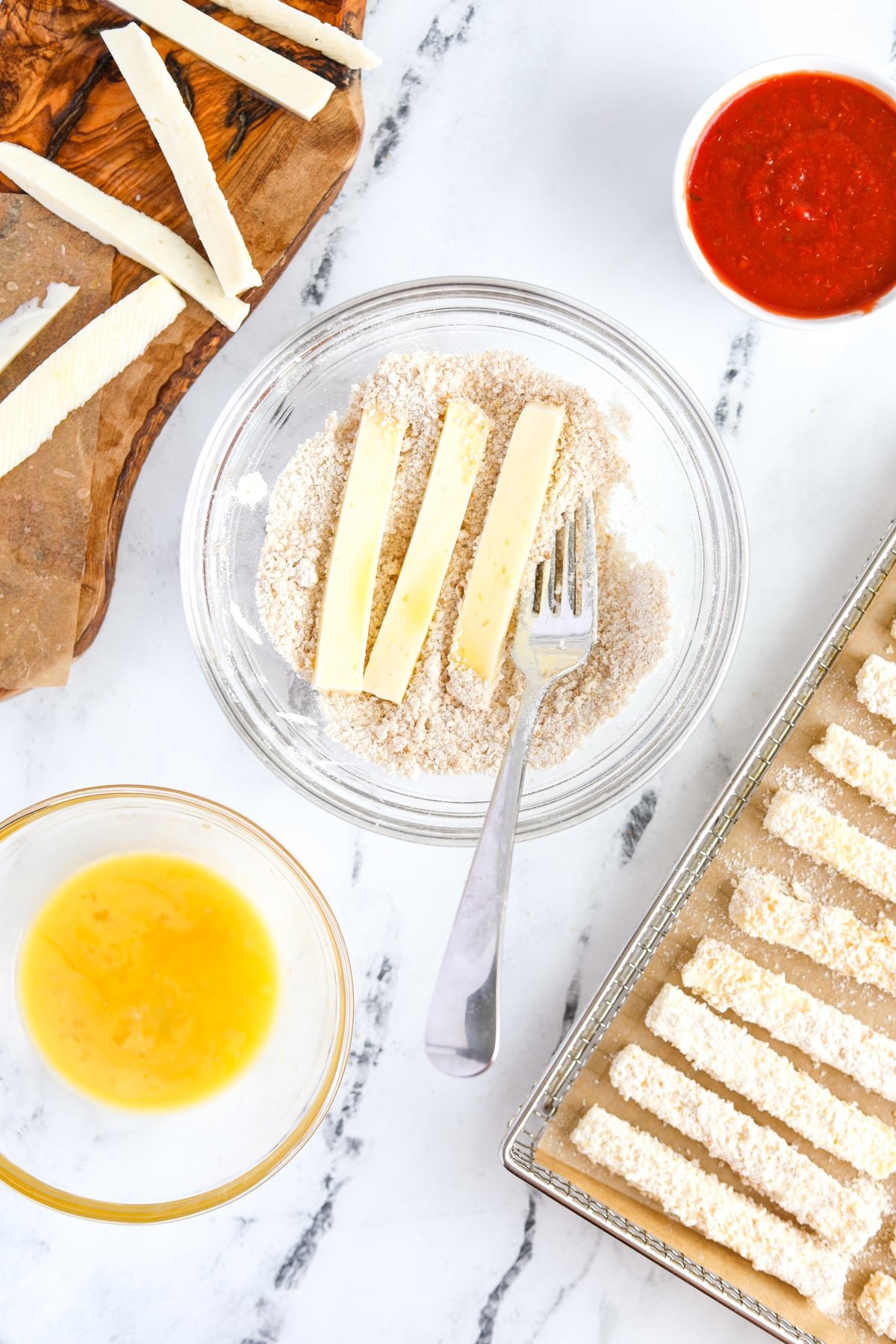 Tossing cheese sticks in a breadcrumb mixture.