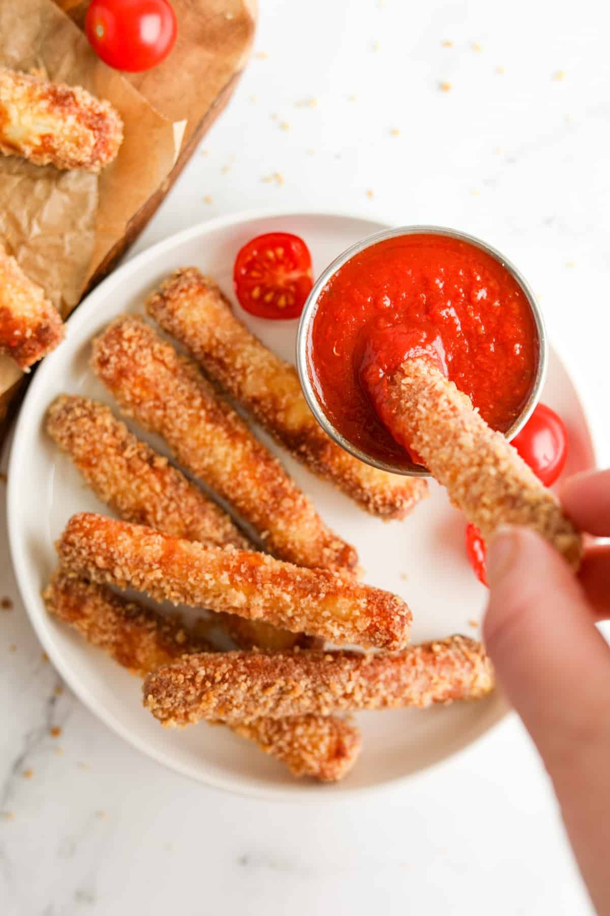 A plate with halloumi fries, and dipping one into a pizza sauce.