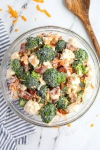 A bowl filled with broccoli and cauliflower salad, topped with cheese and bacon.