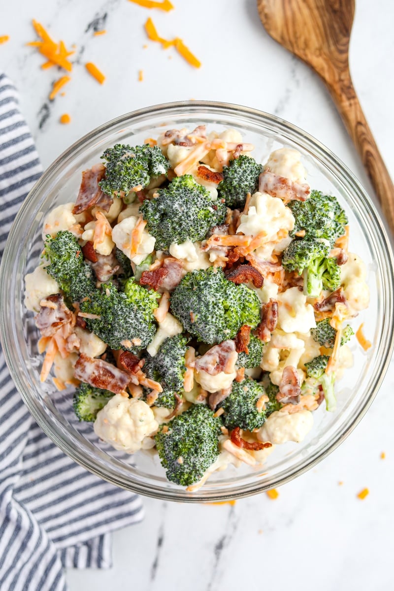 A bowl filled with broccoli and cauliflower salad, topped with cheese and bacon.