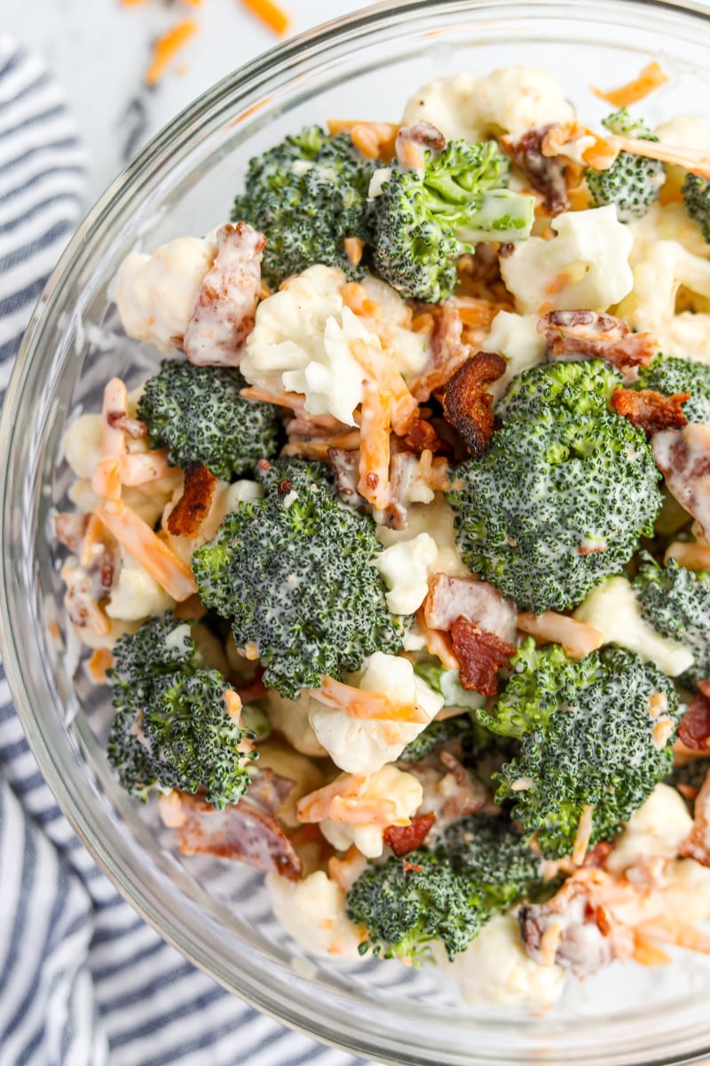 A bowl of broccoli and cauliflower salad, garnished with shredded cheese and bacon.