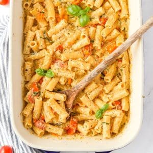 A baking dish with creamy pasta garnished with fresh basil.