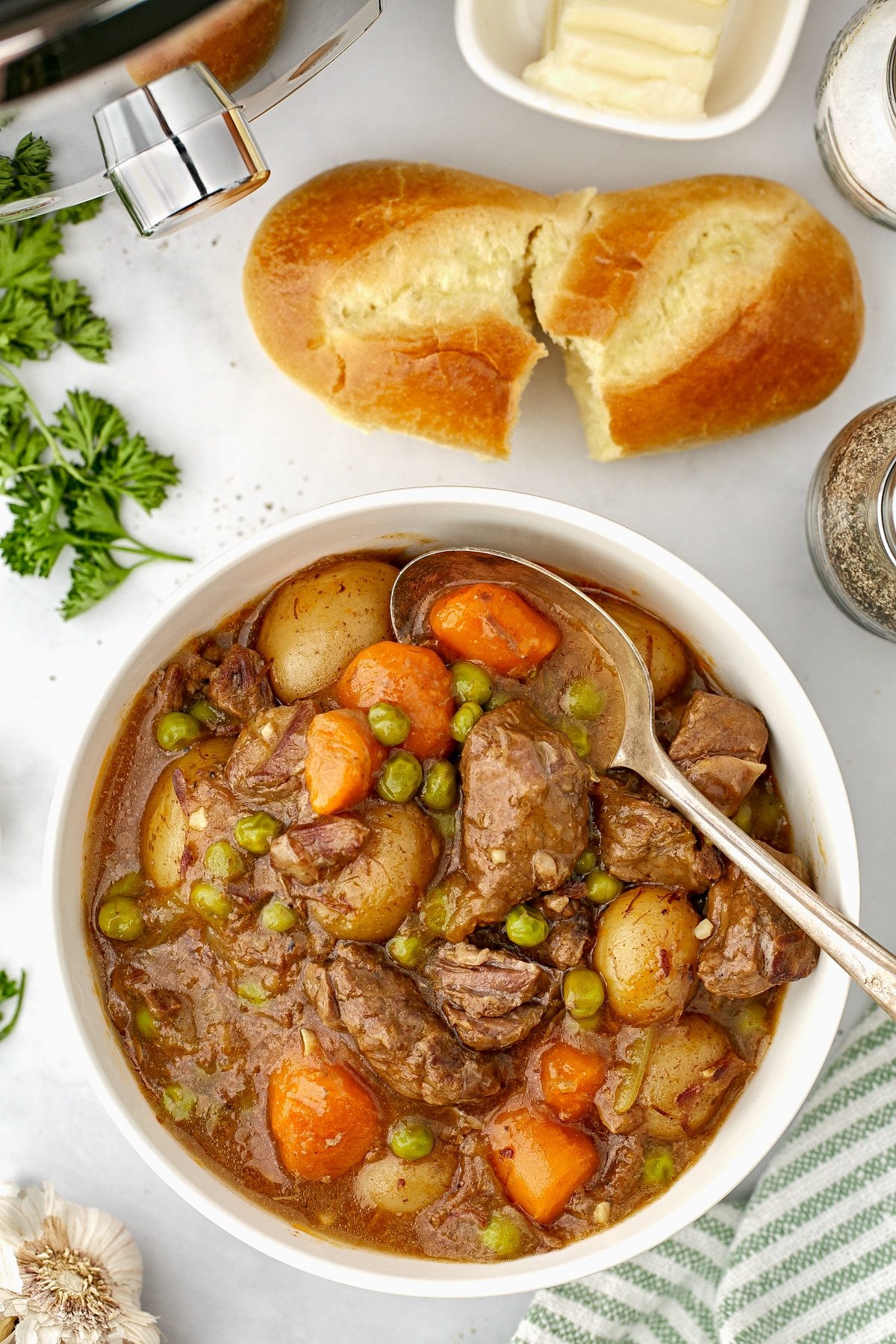 A bowl of beef stew with a small baguette on the side.