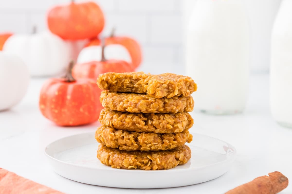 A small stack of pumpkin oatmeal cookies, with fake pumpkins in the background.