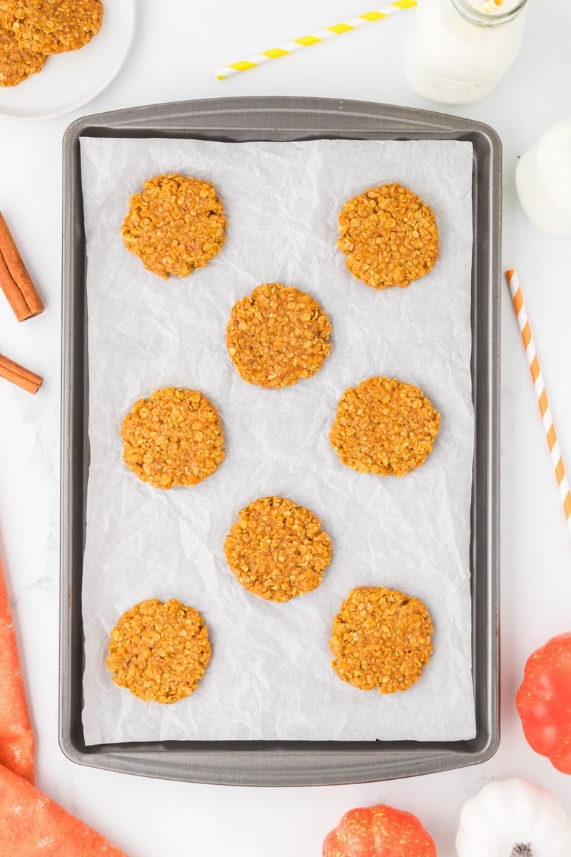 A cookie sheet with flat pumpkin oatmeal cookies on it.