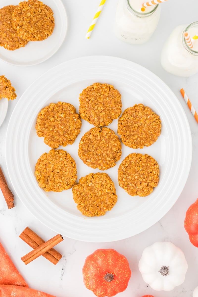 A plateful of flattened pumpkin no bake cookies, with cinnamon sticks and pumpkins around the edge.