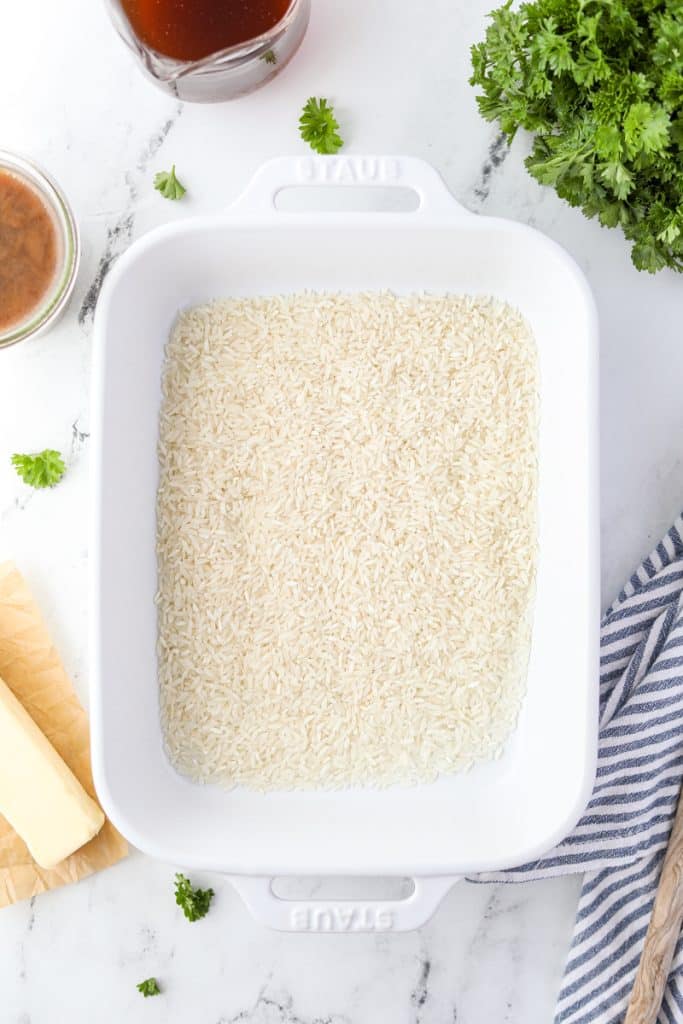 A baking dish with 1 cup of long-grain rice spread out.