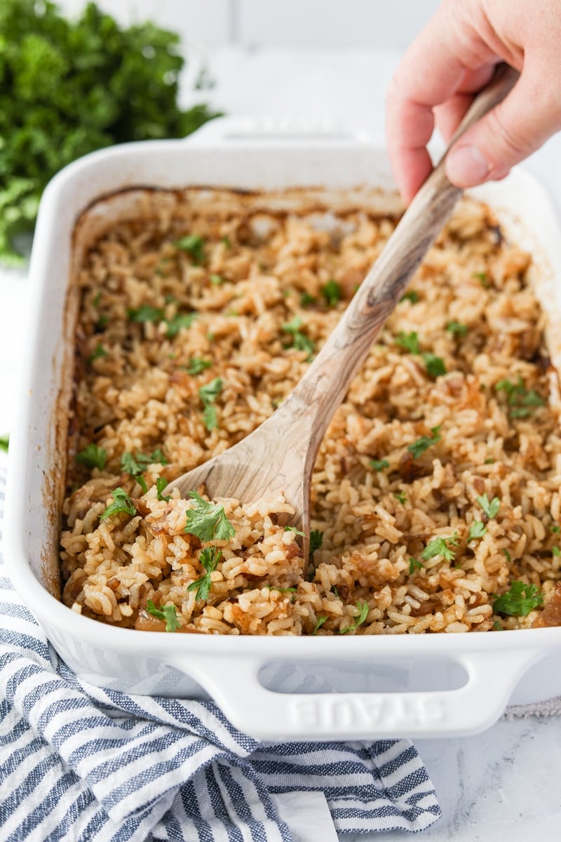 Scooping a portion of rice from a white baking dish.