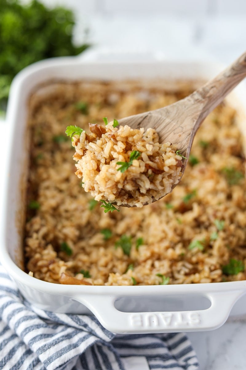 A wooden spoon scooping some rice from a baking dish.