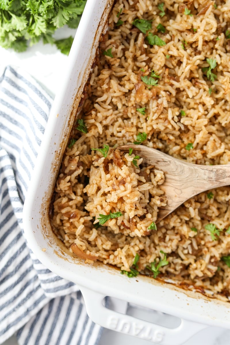 A baking dish filled with fluffy rice, with a wooden spoon scooping a portion.