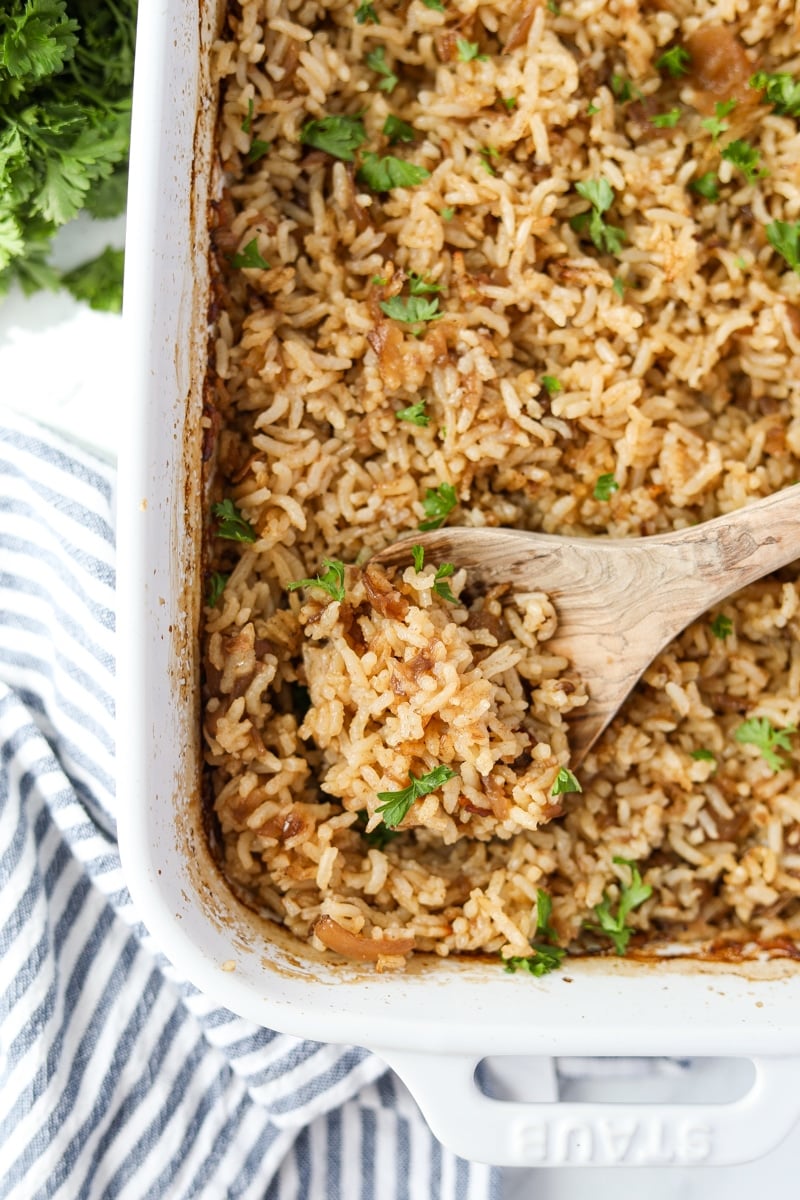 A wooden spoon scooping a portion of rice from a baking dish.