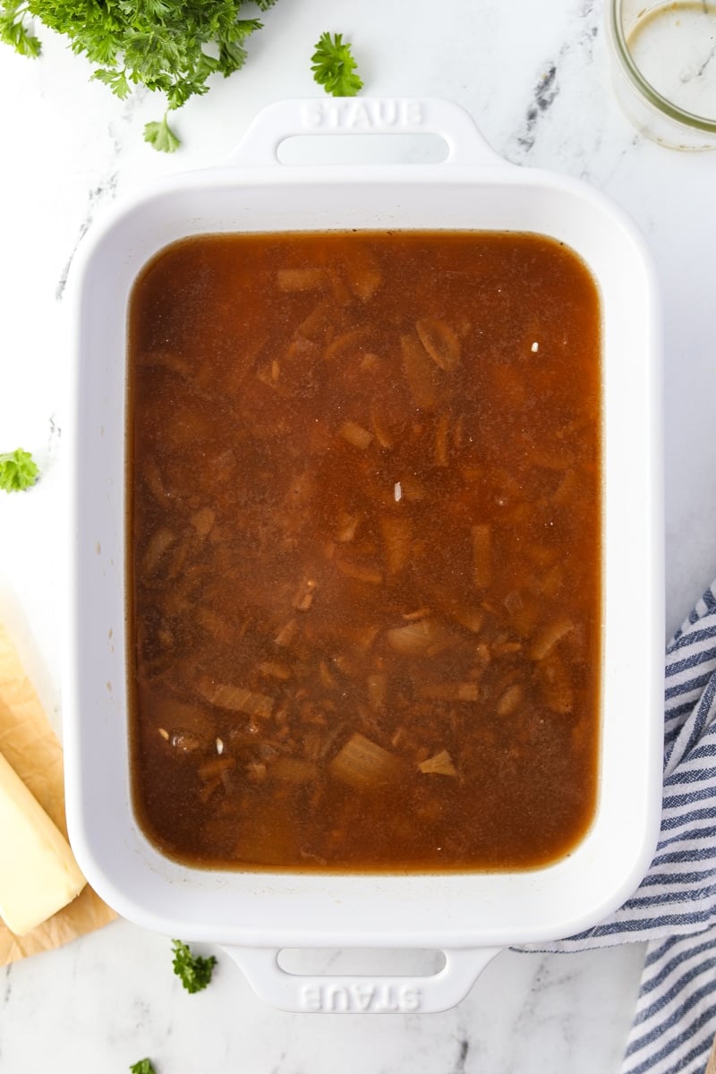 A baking dish with beef broth, onion soup, and rice in it.