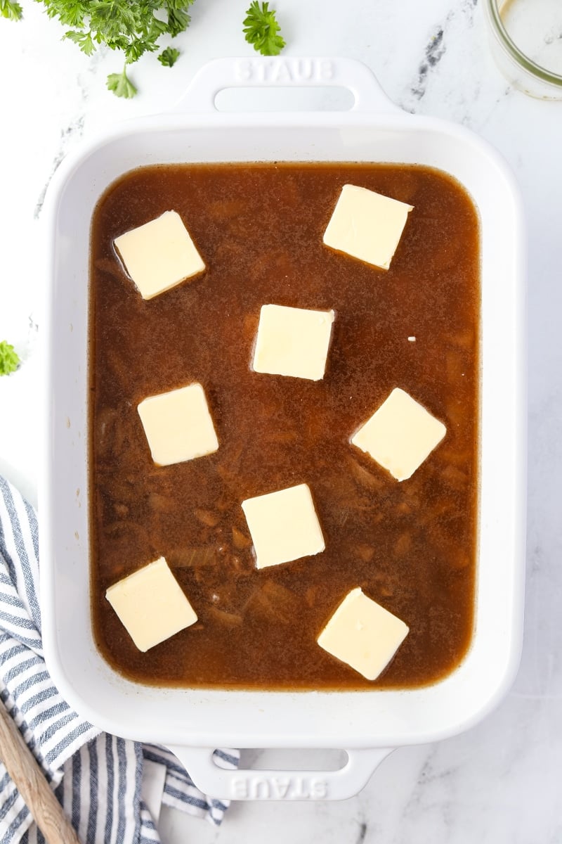 A baking dish with butter pats on top of a liquid and rice mixture.