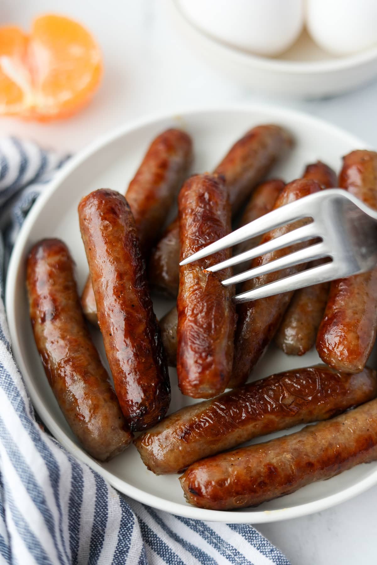 A fork taking a small sausage from a plate.