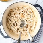 A Dutch Oven with two forks and shredded chicken.